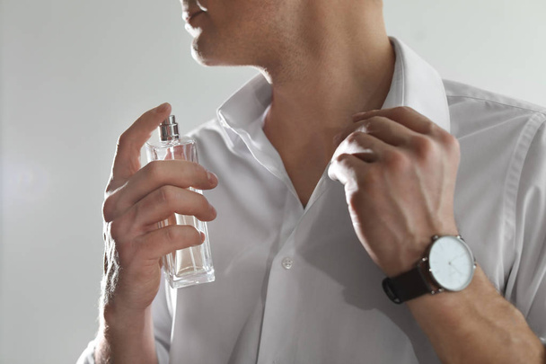 Handsome man applying perfume on neck against light background, closeup - Foto, imagen
