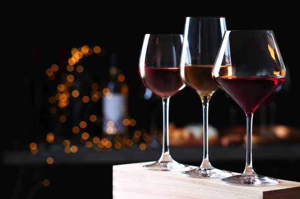 Glasses with different wines on wooden table against defocused lights. Space for text - Foto, Bild