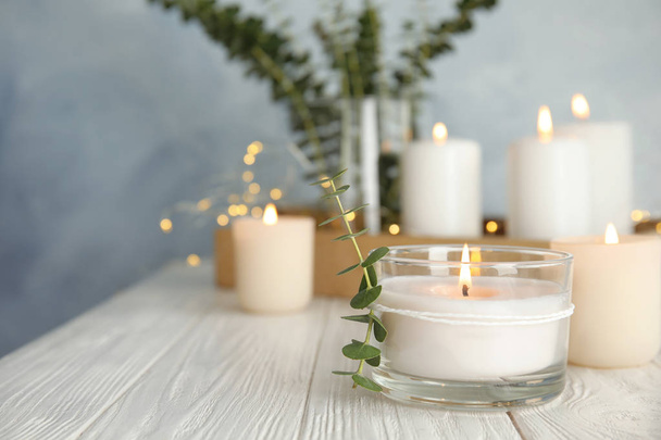 Burning aromatic candle and eucalyptus branch on table. Space for text - Foto, imagen