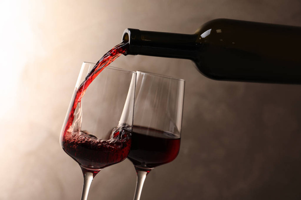 Gieten van wijn van fles in glas op kleur achtergrond - Foto, afbeelding