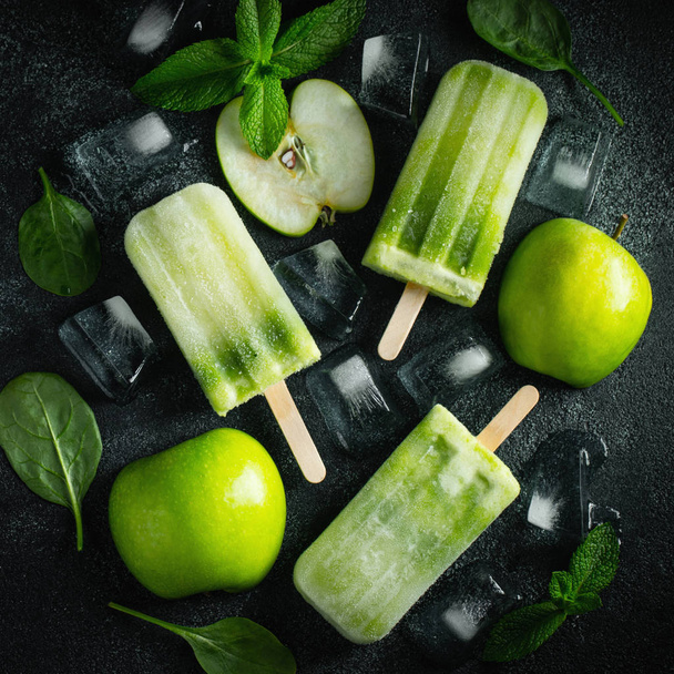 Bright popsicle made of green apple and fresh mint on a dark concrete background. Sweet summer treat. Top view. Flat lay - Photo, Image