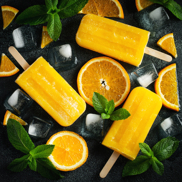 Bright popsicle made of oranges on a dark concrete background. Sweet summer treat. Top view. Flat lay - Photo, Image