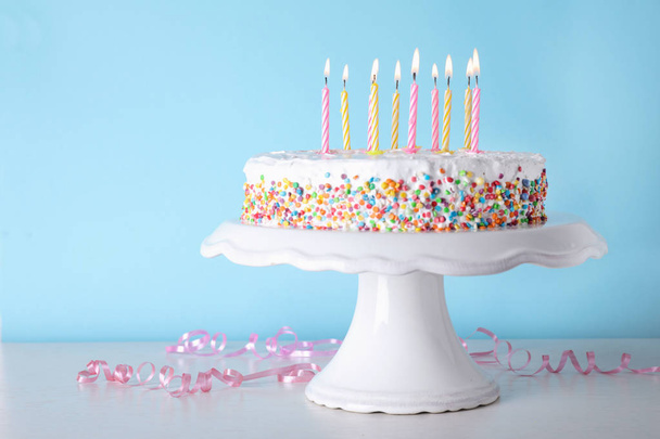 Geburtstagstorte mit brennenden Kerzen auf dem Tisch vor farbigem Hintergrund. Raum für Text - Foto, Bild