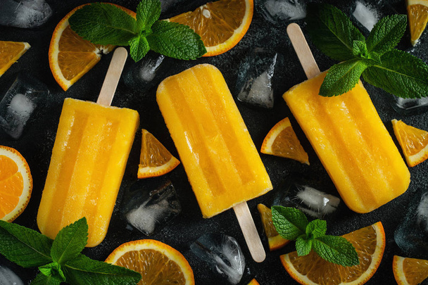 Bright popsicle made of oranges on a dark concrete background. Sweet summer treat. Top view. Flat lay - Photo, Image