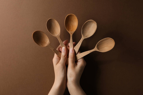 Woman holding empty wooden spoons on color background, closeup - Фото, зображення