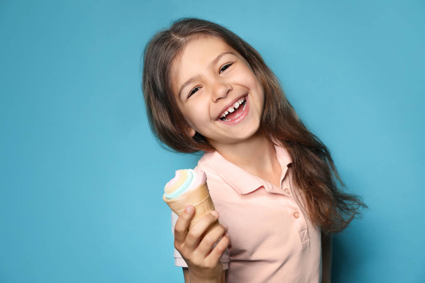 Adorable little girl with delicious ice cream against color background, space for text - 写真・画像