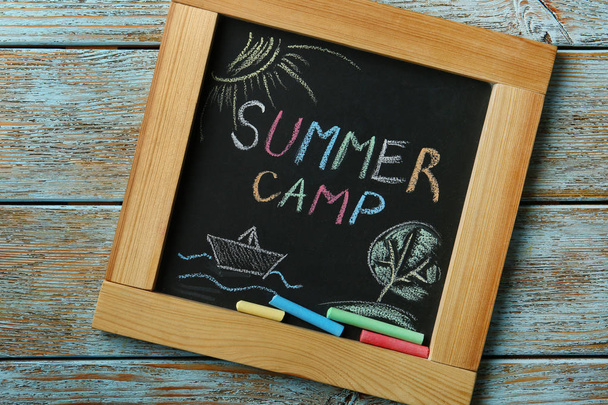 Blackboard with text SUMMER CAMP, drawings and chalk sticks on wooden background, top view - Foto, immagini