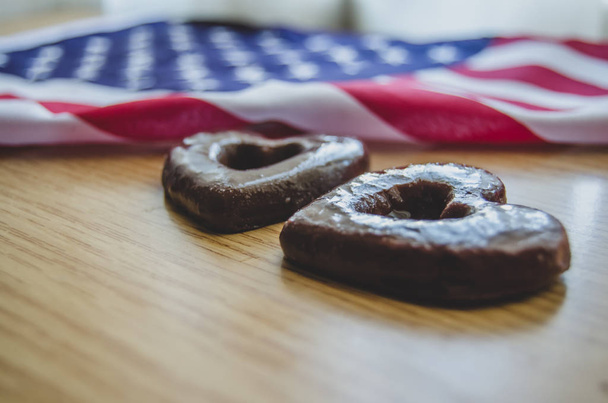 木製テーブルの幸せな記念日に2つのハート形のビスケットとアメリカの旗. - 写真・画像