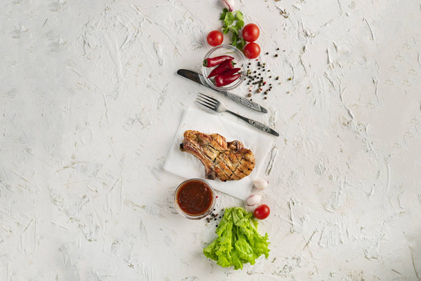 μαγειρεμένο κρέας διάταξη, μπαχαρικά, φύλλα μαρουλιού, ντομάτα, πιπέρι και σάλτσα που γύρω, επιτραπέζια σκεύη, μαχαίρι, πιρούνια - Φωτογραφία, εικόνα