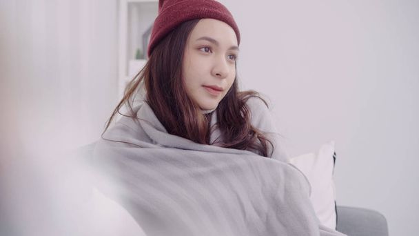 Asian woman feel headache wrapped in grey blanket blow the nose and use tissue while lying on couch when relax in living room at home. Lifestyle women in Christmas and New year holidays concept. - Photo, Image