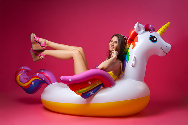 Yaz moda güzel kadın yaz giysileri eğlenmek, gülümseme ve balon ile poz üzerinde Unicorn float izole pembe arka plan - Fotoğraf, Görsel