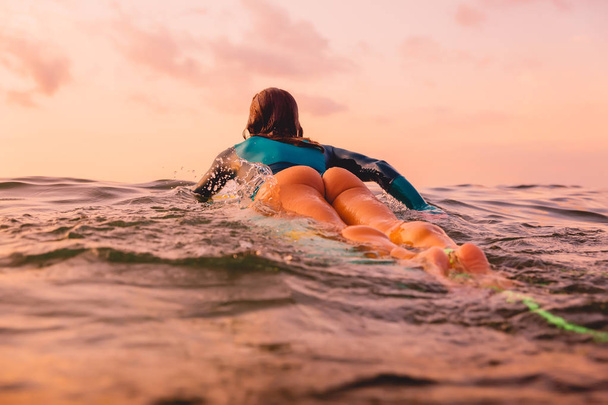 Красивая серфингистка на доске для сёрфинга, плавающая в океане. Серфинг на закате
 - Фото, изображение