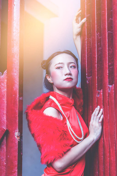 恥ずかしがり屋の中国人女性が赤い木製のドアの後ろに隠れている - 写真・画像