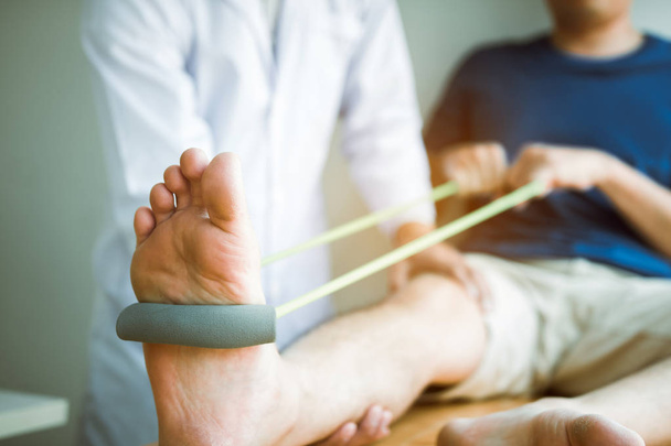 Ο ασθενής χρησιμοποιεί ζώνη αντίστασης που απλώνεται στο πόδι του με σωματική - Φωτογραφία, εικόνα
