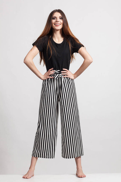 Photo of a beautiful slim woman in full growth, dressed in a black blouse and striped pants - Foto, imagen
