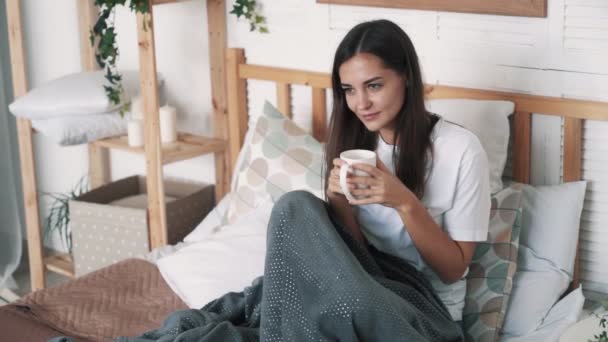 Sensual girl sits on bed, drinks coffee, relaxes and smiles, slow motion - Felvétel, videó