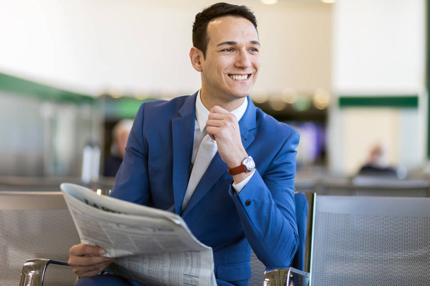 Professional handsome businessman reading a newspaper and resting while sitting in the departure lounge - Foto, Imagen
