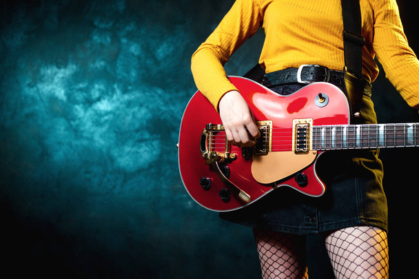 Foto de cerca de piernas de mujer hipster joven y guitarra roja en luces de neón. El músico de rock toca la guitarra eléctrica. Concepto de estilo de los 90
. - Foto, imagen