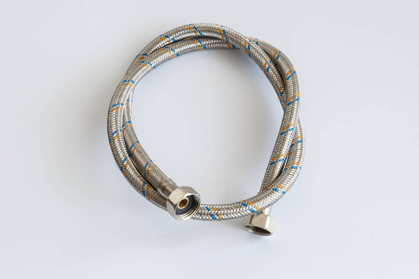 Flexible water pipe in metal braid on white background twisted into a ring - Foto, imagen