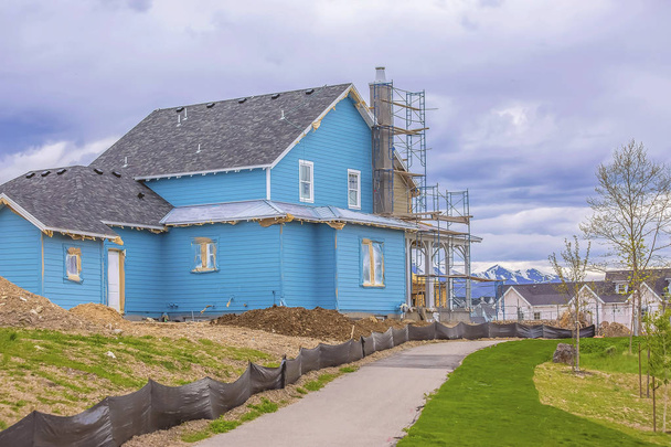 Casa azul en construcción con andamios contra la montaña y el cielo nublado
 - Foto, Imagen
