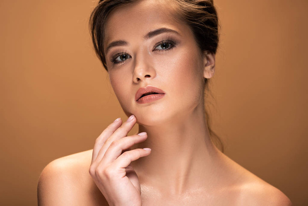young beautiful naked woman with shiny makeup touching face isolated on beige - Fotografie, Obrázek