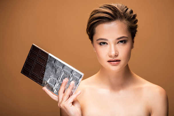 giovane donna nuda con barretta di cioccolato in lamina d'argento isolata su beige
 - Foto, immagini