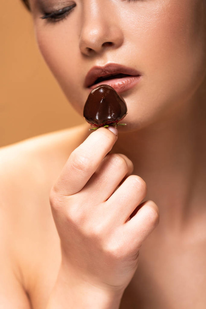 young naked woman looking at strawberry in melted chocolate isolated on beige - Photo, Image