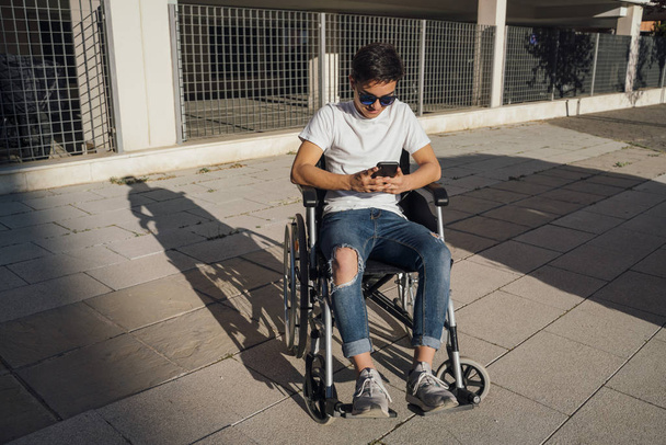 Portret van een leuke jongen zittend op een rolstoel buiten - Foto, afbeelding