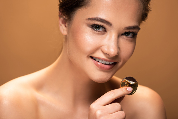 smiling naked young woman holding chocolate coin in golden foil isolated on beige - Фото, изображение