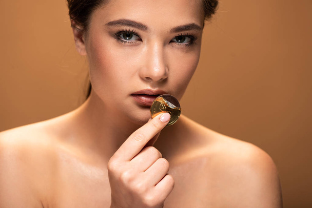 jeune femme nue tenant pièce de chocolat en feuille d'or près des lèvres isolées sur beige
 - Photo, image