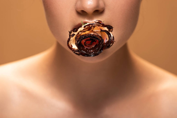 oříznutý pohled na nahou ženu růži v ústech pokrytý rozpuštěnou čokoládou izolovanou na béžové - Fotografie, Obrázek