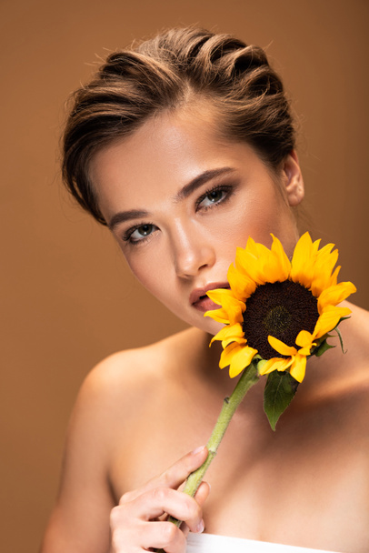 krásná mladá nahá žena se žlutou slunečnicou izolovanou na hnědém - Fotografie, Obrázek