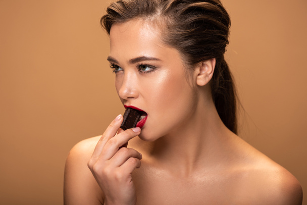 όμορφη γυμνή γυναίκα τρώγοντας κομμάτι σοκολάτας απομονωθεί σε μπεζ - Φωτογραφία, εικόνα