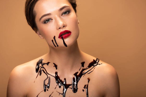 dirty and beautiful naked woman with red lips and chocolate spills on skin isolated on beige - 写真・画像