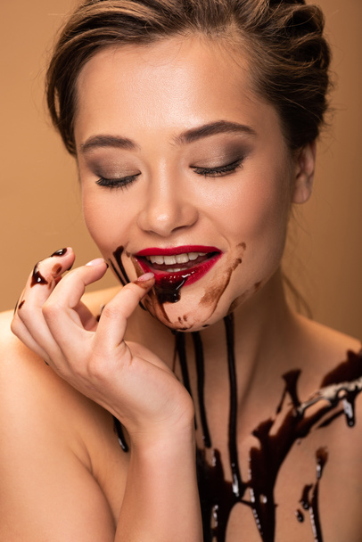 smiling naked woman with red lips and chocolate spills on skin isolated on beige - Foto, Imagem