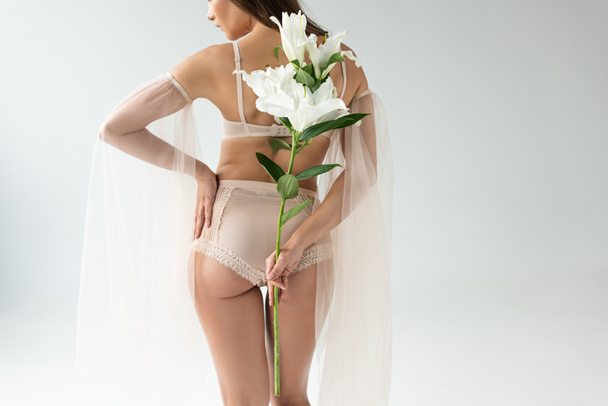 back view of delicate young woman in beige lingerie and mesh sleeves holding bouquet of lilies isolated on white - Fotoğraf, Görsel