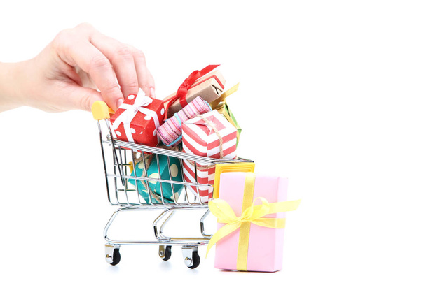 Female hand holding small shopping cart with gift boxes isolated on white background - Photo, Image