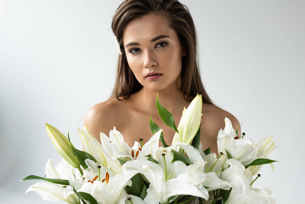 tender naked young woman looking at camera near white lilies  - Photo, Image