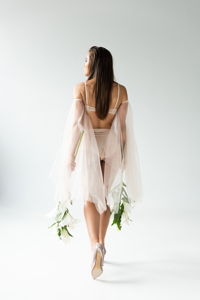 back view of tender young woman walking with lilies isolated on white - Foto, afbeelding