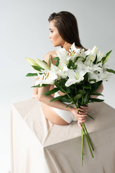 Rückseite der zarten jungen Frau im weißen Spitzenbody mit Lilienstrauß auf weißem Hintergrund - Foto, Bild