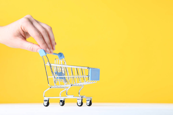 Small shopping cart with female hand on yellow background - Valokuva, kuva