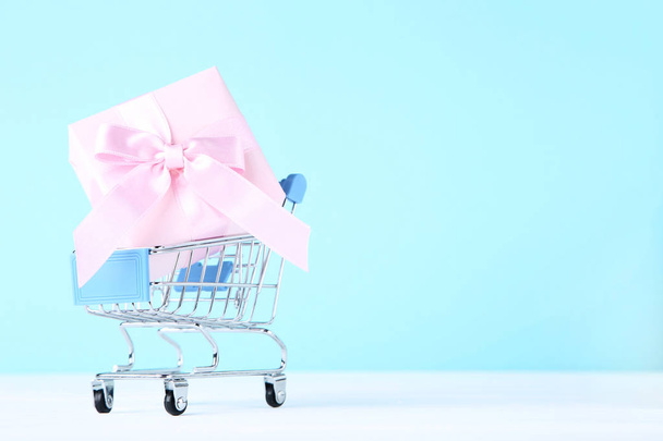 Small shopping cart with gift box on blue background - Фото, зображення