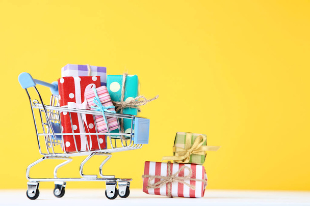 Small shopping cart with gift boxes on yellow background - Foto, immagini