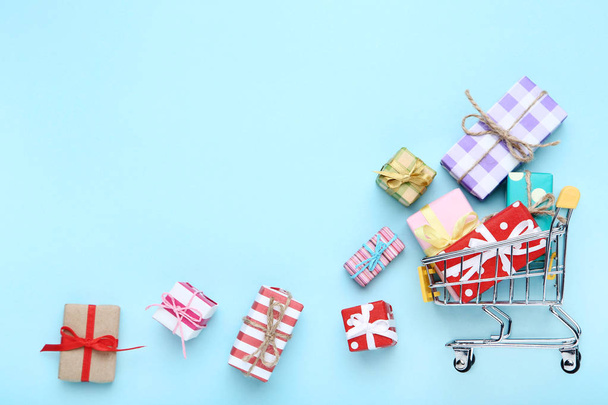 Small shopping cart with gift boxes on blue background - Foto, Bild