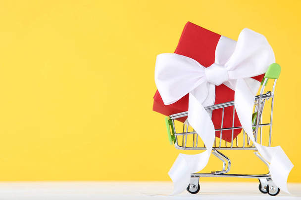 Small shopping cart with gift box on yellow background - Fotografie, Obrázek