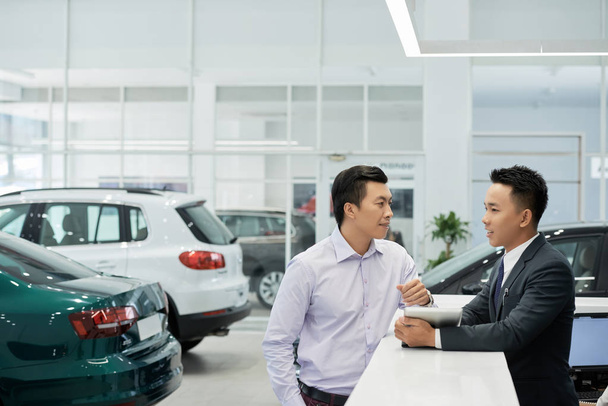 Ζευγάρι βιετναμέζικος πελάτης αντιπροσωπεία αυτοκινήτων μιλάει με τον διευθυντή πωλήσεων - Φωτογραφία, εικόνα