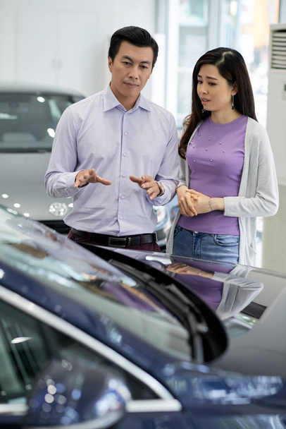 Asiatico coppia discutere auto vantaggi e svantaggi in auto concessionaria
 - Foto, immagini