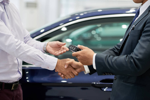 Продавец дает ключи от машины клиенту и пожимает ему руку
 - Фото, изображение