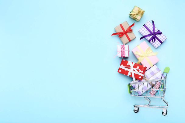 Small shopping cart with gift boxes on blue background - Foto, afbeelding