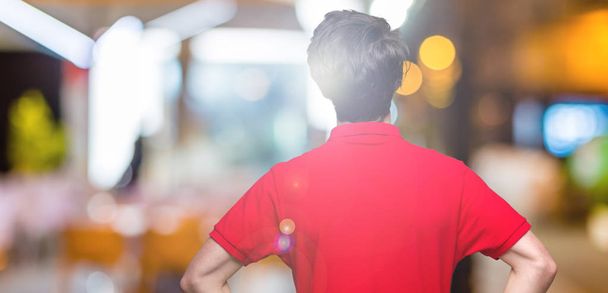 Όμορφος νεαρός φορώντας κόκκινο t-shirt πάνω από το απομονωμένο φόντο στέκεται κοιτάζοντας προς τα πίσω μακριά με τα χέρια στο σώμα - Φωτογραφία, εικόνα